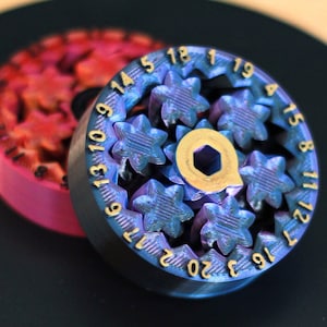 Op de afbeelding: Een close-up van een blauwe en gouden metalen tandwiel met de nummers 13 tot 20 rond de rand. Het tandwiel heeft een stervormig ontwerp en wordt omringd door andere tandwielen.