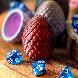 May include: A red dragon egg-shaped dice with a textured surface, surrounded by blue dice with white numbers. The dice are on a wooden surface.