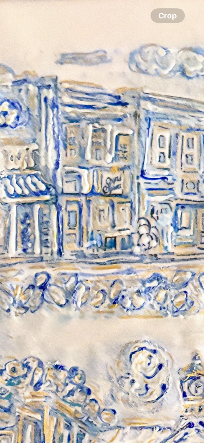 Op de afbeelding: Een gedetailleerd, getextureerd reli&euml;fsculptuur dat een straatbeeld weergeeft met gebouwen in blauw, wit en goud. Het kunstwerk toont architectonische details, winkelpuien en decoratieve elementen, waardoor een driedimensionaal effect ontstaat.