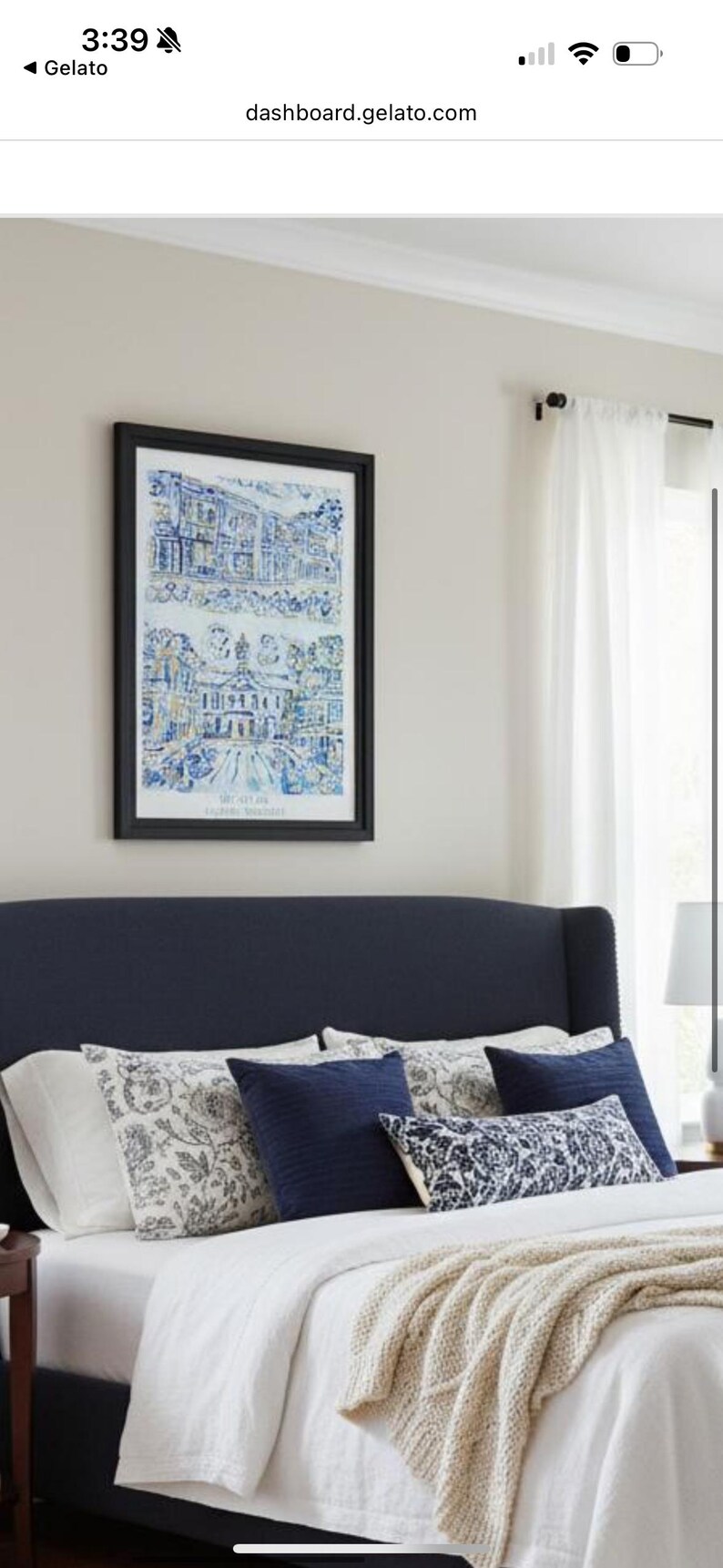 Op de afbeelding: Een slaapkamerinterieur met een marineblauw hoofdbord, wit beddengoed en decoratieve kussens. Een ingelijste prent met blauw-witte architectonische illustraties hangt boven het bed. Een beige sprei voegt textuur toe.