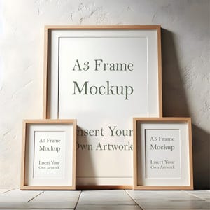 May include: Three wooden picture frames, one large A3 size and two smaller A5 size, are arranged on a light wood surface. The frames are all natural wood colour and have a white mount. The text "A3 Frame Mockup" is printed on the large frame, and the text "A5 Frame Mockup" is printed on the smaller frames. The text "Insert Your Own Artwork" is printed below the mockup text on each frame.