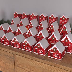 Puede incluir: Un calendario de adviento navideño rojo y blanco con forma de pueblo de casas con puertas numeradas. Las casas están dispuestas en forma de pirámide.
