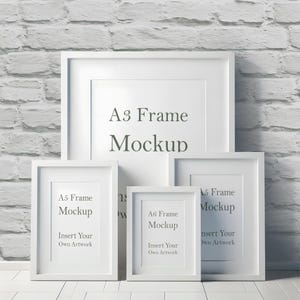 May include: Four white picture frames of different sizes, with the largest frame labeled "A3 Frame Mockup". The smaller frames are labeled "A5 Frame Mockup" and "A6 Frame Mockup". Each frame has a white mat and a white background.