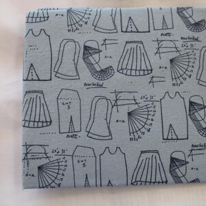 May include: A light blue fabric with black line drawings of various clothing patterns, including skirts, dresses, and tops. The fabric also includes text such as "note", "cut 3", and "marked".