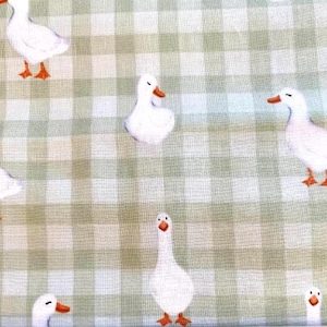 May include: A fabric featuring a repeating pattern of white ducks with orange beaks and feet, set against a light green and white checkered background. The ducks are depicted in various poses, including standing and facing different directions.