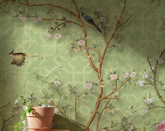 Op de afbeelding: Een groene behang met een bloemenpatroon met delicate roze bloemen en bruine takken. Twee vogels zitten op de takken. Een kleine plant in een pot staat op een houten kruk voor de behang.