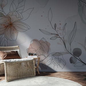 Pu&ograve; includere: Una sedia in vimini con un cuscino marrone si trova di fronte a un muro con un design floreale. Il design presenta delicati disegni di fiori e foglie in linea nera con lavaggi ad acquerello in tonalit&agrave; rosa e grigio.