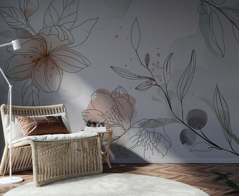 Pu&ograve; includere: Una sedia in vimini con un cuscino marrone si trova di fronte a un muro con un design floreale. Il design presenta delicati disegni di fiori e foglie in linea nera con lavaggi ad acquerello in tonalit&agrave; rosa e grigio.