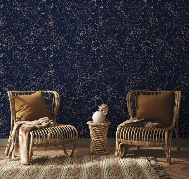 Peut inclure: Deux chaises en osier avec des coussins marrons et une couverture pos&eacute;es devant un mur bleu fonc&eacute; avec un motif floral dor&eacute;. Une petite table d'appoint en osier avec un vase en c&eacute;ramique blanc contenant un bouquet de fleurs se trouve entre les chaises.
