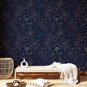 Peut inclure: Un papier peint bleu marine avec un motif floral dor&eacute; repr&eacute;sentant des roses et des lys. Le papier peint est pr&eacute;sent&eacute; dans une pi&egrave;ce avec un banc en bois, un panier en osier et une couverture blanche.