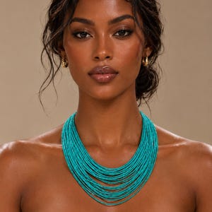Peut inclure: Un collier multi-brins composé de nombreux cordons fins de perles bleu turquoise vif, superposés pour créer un effet de collerette large et en cascade reposant sur les clavicules, accompagné de petites boucles d'oreilles créoles dorées.