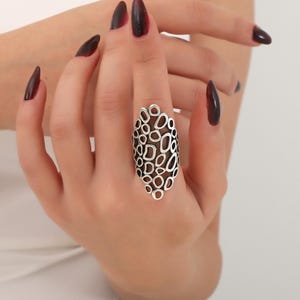 May include: A silver ring with a unique design featuring a cluster of interconnected circles and ovals. The ring is worn on a finger with dark red nail polish.