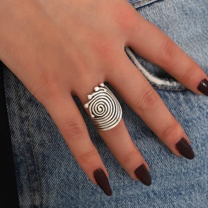 May include: Silver ring with a spiral design. The ring is wide and has a textured surface.