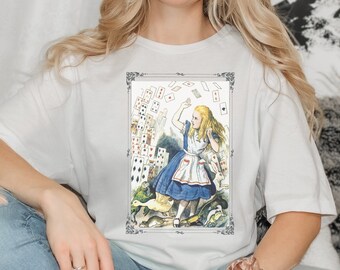 May include: A white t-shirt with a vintage illustration of Alice from Alice in Wonderland surrounded by playing cards. The illustration is framed in a decorative border.