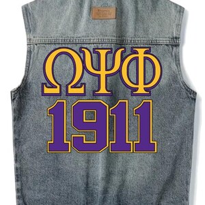 May include: A sleeveless denim jacket with a faded wash. The back features the Greek letters Omega, Psi, and Phi in gold with a purple outline, above the number 1911 in purple with a gold outline. A small brown tag is at the top.