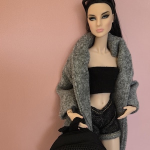 May include: A fashion doll wearing a grey coat, a black bandeau top, denim shorts, and a black backpack.