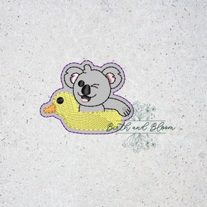 May include: Embroidered design of a gray koala wearing a yellow duck floaty, with a winking eye. The design is perfect for a baby shower or nursery.