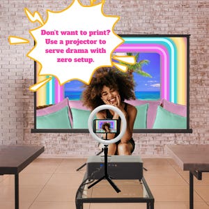 May include: A woman smiles in front of a screen displaying a tropical scene. A ring light with a phone is positioned in front of her. A projector sits on a small table. Text in a speech bubble reads: "Don't want to print? Use a projector to serve drama with zero setup."