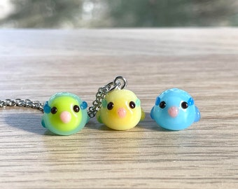 May include: Three glass charms shaped like pufferfish, each with a different color: green, yellow, and blue. The charms are on a silver chain.