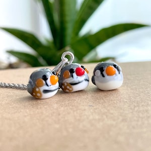 May include: Three glass bird charms with black, white, orange, and red details. The charms are on a silver chain.