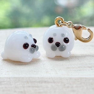 May include: Two white glass seal charms, one with a gold clasp. The charms have black eyes and grey noses.