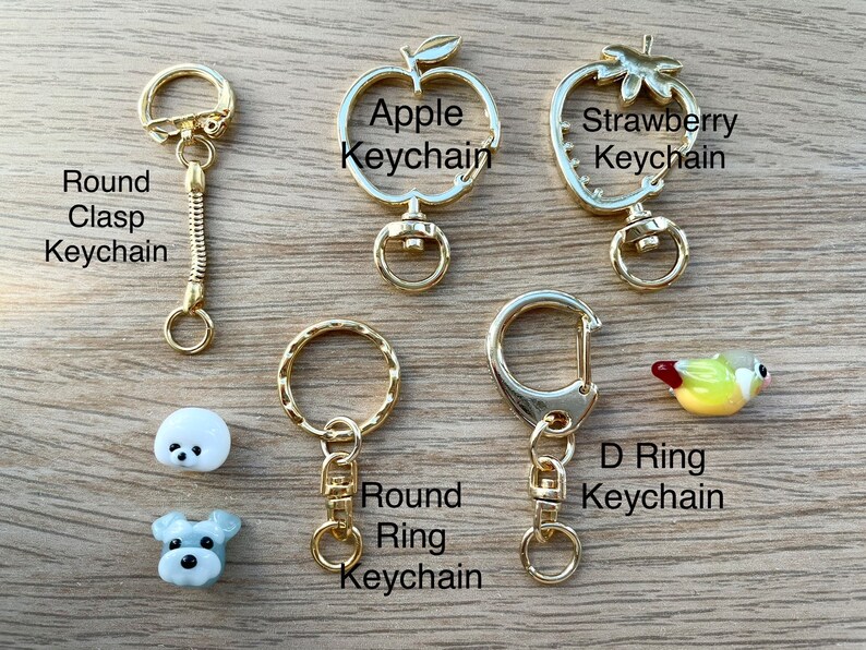 May include: Assortment of gold keychains with different designs, including a round clasp, a round ring, a D ring, an apple, and a strawberry. There are also two small glass figurines of dogs.