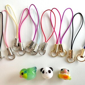 Puede incluir: Surtido de abalorios para tel&eacute;fono de colores con anillos y cuentas de metal. Los abalorios est&aacute;n hechos de cuerda fina y est&aacute;n disponibles en una variedad de colores, incluyendo rosa, amarillo, azul, rojo, morado, negro y blanco. Los abalorios se muestran sobre una superficie blanca con tres peque&ntilde;as figuritas decorativas.