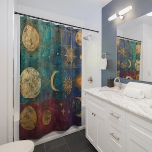 May include: A celestial-themed shower curtain with a teal, blue, and burgundy color scheme. The design features gold suns, moons, stars, and other celestial bodies. The curtain is hanging in a bathroom with white cabinets and a marble countertop.