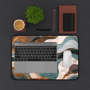 May include: A modern desk setup featuring a laptop, mouse, and a decorative mousepad with an abstract design in shades of gold, teal, and white. A coffee cup, plant, notebook, and pens complete the workspace.