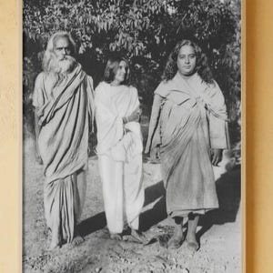 May include: A framed black and white photograph showing three people in traditional attire. The person on the left has a long white beard and draped fabric. The person in the middle is in white, and the person on the right is wearing draped fabric.