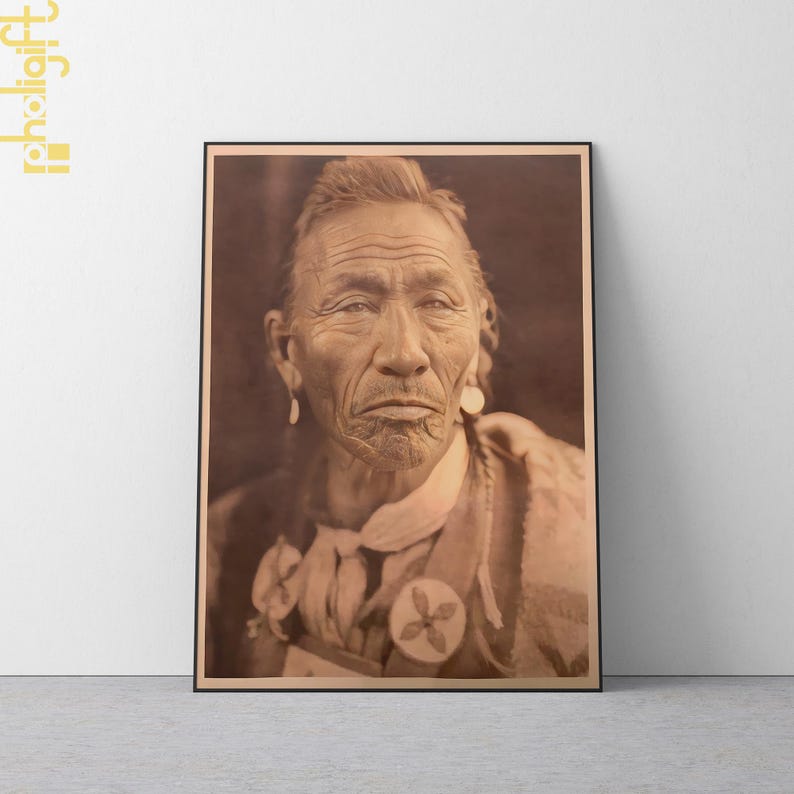 May include: Framed sepia-toned portrait of an elderly Native American man. The man has deep wrinkles, long hair, and is wearing earrings and a decorative medallion. The image is in a black frame.