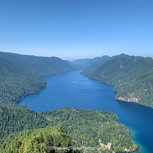 May include: An aerial view of a deep blue lake surrounded by lush green mountains. The lake is narrow and winding, creating a scenic vista.