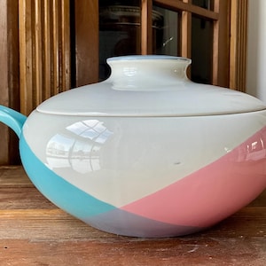 May include: A large, white ceramic serving dish with a lid. The dish features a diagonal stripe design in light blue and pink. The handle and spout are also painted in light blue and pink.