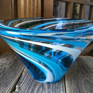 May include: A large, blue and white glass bowl with a swirling pattern. The bowl is made of clear glass with blue and white stripes that swirl around the bowl.