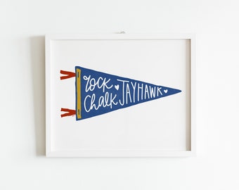 May include: A blue pennant with the text "Rock Chalk Jayhawk" in white script with two small hearts. The pennant is framed in a white frame.