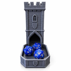 Puede incluir: Una torre de dados gris impresa en 3D con textura de ladrillo de piedra, parte superior almenada y un emblema de escudo. La torre tiene una abertura arqueada en la base que conduce a una bandeja con tres dados azules de veinte caras.