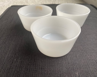 May include: Three white ceramic bowls, possibly for serving desserts or dips, are arranged on a black textured surface.