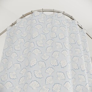 May include: A shower curtain featuring a pattern of white seashells on a light blue striped background. The curtain is suspended from a curved, silver shower rail. The design has a coastal or seaside theme.