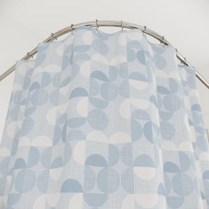 May include: A shower curtain hanging from a curved metal rod with silver rings. The fabric features a repeating geometric pattern of semi-circles and circles in shades of light blue, white, and a fine blue grid texture on a pale blue background.