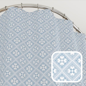 May include: A light blue shower curtain with a repeating geometric pattern of white and light blue star-like shapes within a diamond grid. The curtain hangs from a silver metal rod with hooks.