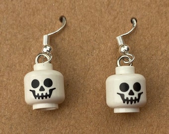May include: A pair of silver skeleton head earrings. The earrings are made of white plastic and feature a black skull design.