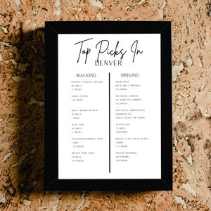 Op de afbeelding: Een zwart omkaderde print met de tekst "Top Picks In Denver" in elegant schrift. De print geeft wandel- en autoritten weer, waaronder musea, tuinen en rondleidingen. De achtergrond is een getextureerd, lichtbruin oppervlak.