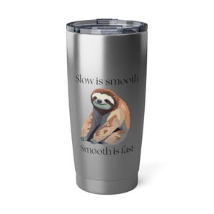 May include: A stainless steel tumbler with a black lid. The tumbler features a cartoon sloth illustration in shades of brown and tan. The text "Slow is smooth, Smooth is fast" is printed above and below the sloth.