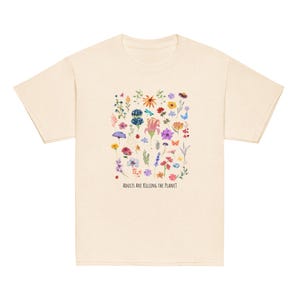 May include: Cream-coloured t-shirt with a colourful floral design featuring various flowers and the text "ADULTS ARE KILLING THE PLANET" in black. The shirt has short sleeves and a crew neck.