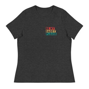 May include: Dark grey t-shirt featuring the text "BE MY DADDY PLEASE" in a retro colour block design. The text is stacked vertically, with each word in a different colour: red, yellow, and teal. The shirt has a relaxed fit.