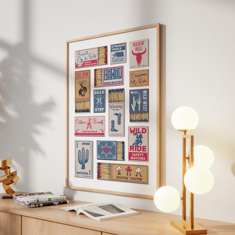 A trendy art piece displaying old matchbook designs with a Western theme. The matchboxes feature graphics and text such as "Yee Haw" and "Raisin' Hell." The frame is light brown, and the print is mounted on a white wall.
