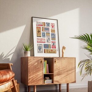 A eclectic print displaying retro matchbook designs with americana themes. The artwork includes illustrations and text, such as cacti, boots, and the words "Born To Be Wild" The print is displayed on a wooden cabinet.