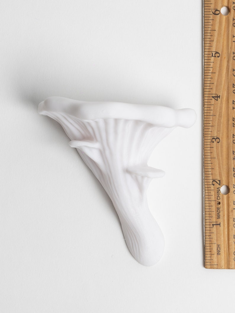 Op de afbeelding: Witte keramische paddenstoelensculptuur met een gedetailleerd, gestructureerd oppervlak. De sculptuur is ongeveer 7,5 cm hoog.