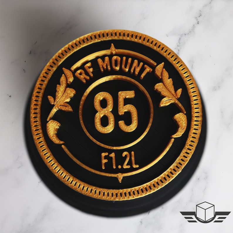 Pu&ograve; includere: Un tappo per obiettivo della fotocamera rotondo nero e oro con la scritta "RF MOUNT 85 F1.2L" stampata su di esso.