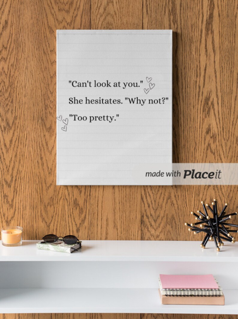 May include: A white canvas with a handwritten quote: "Can't look at you." She hesitates. "Why not?" "Too pretty." The canvas is hanging on a wood wall above a white shelf with a candle, sunglasses, a book, and a pink notebook.